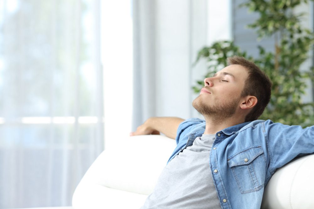 young man sitting on the couch, leaning back and feeling calm and serene.