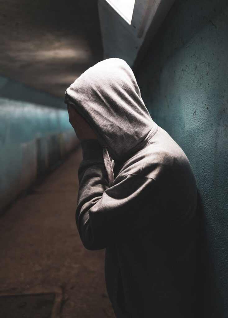 person wearing a hooded sweatshirt holding their face in their hands, upset. Drug Addiction