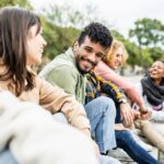 Group of diverse young adults sitting outdoors, smiling and talking together in a relaxed, friendly atmosphere.
