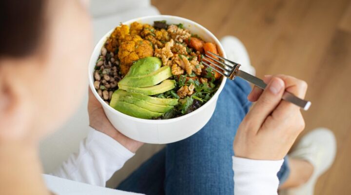 Person holding a bowl of healthy food, including avocado, greens, beans, and roasted vegetables, representing balanced nutrition and wellness.