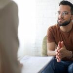 Man in therapy session attentively listening and engaging in conversation with a mental health professional.