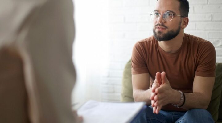 Man in therapy session attentively listening and engaging in conversation with a mental health professional.