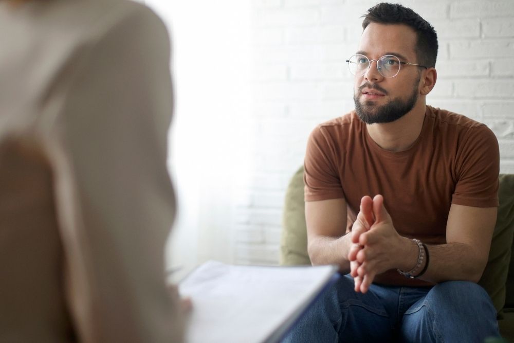 Man in therapy session attentively listening and engaging in conversation with a mental health professional.