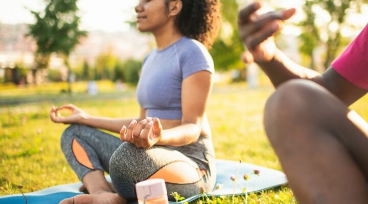 Stone River - What Healthy Self-Care Really Looks Like. A woman out of focus sits on a blue yoga mat assuming a sitting yoga pose.