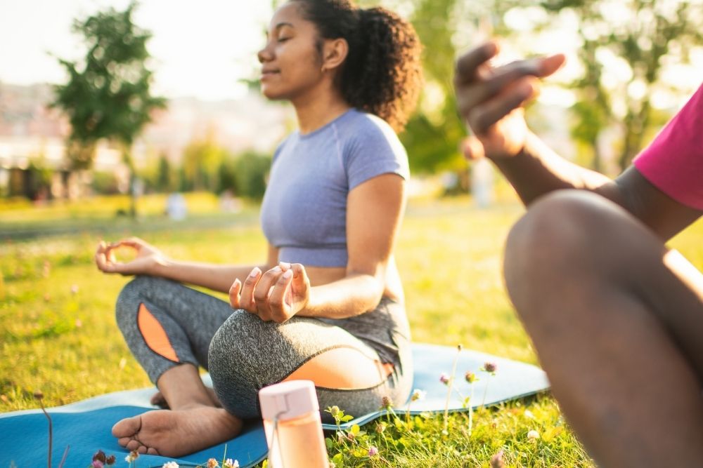 Stone River - What Healthy Self-Care Really Looks Like. A woman out of focus sits on a blue yoga mat assuming a sitting yoga pose.