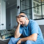 Person sitting on a couch with head in hand, appearing stressed or overwhelmed in a quiet home setting.