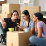 Stone River - How to Create a Sober-Friendly Home. Three women sit around a turned over card board box looking at a phone. They are in the process of moving.