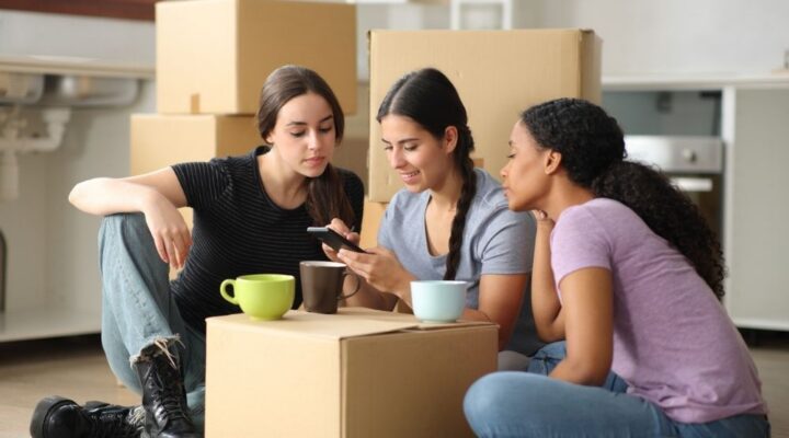 Stone River - How to Create a Sober-Friendly Home. Three women sit around a turned over card board box looking at a phone. They are in the process of moving.