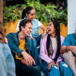 Stone River - The Language You Use Matters - Edited. Friends sitting on a bench in an outdoor environment smile and laugh with one another in conversation.