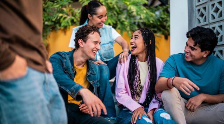 Stone River - The Language You Use Matters - Edited. Friends sitting on a bench in an outdoor environment smile and laugh with one another in conversation.