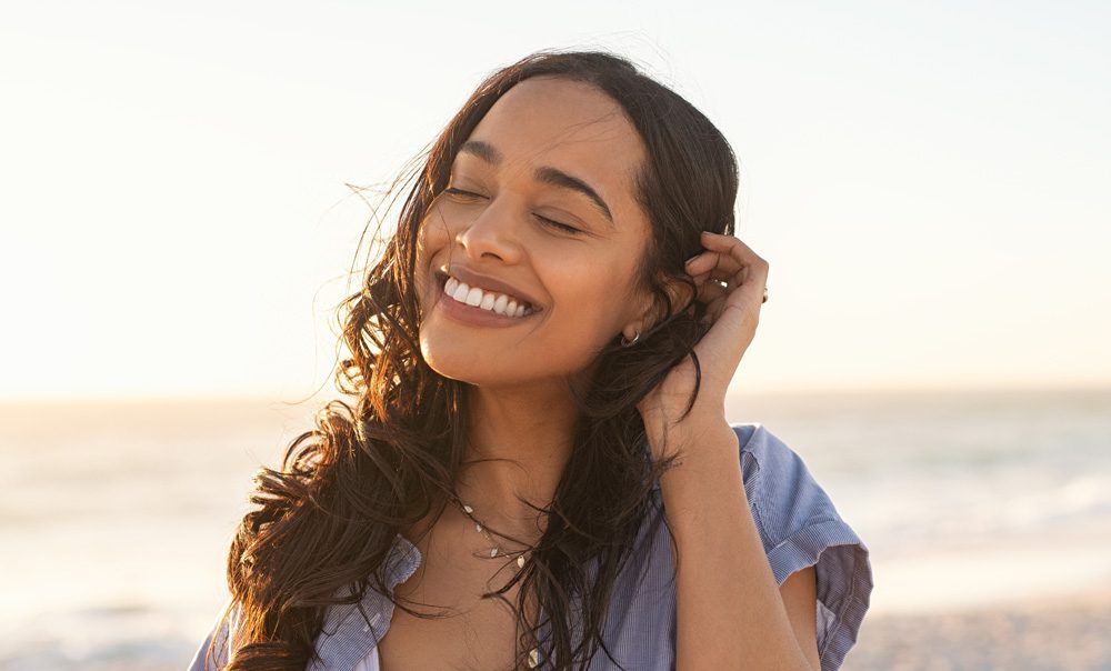 portrait of a woman smiling with her eyes closed, outdoors on a beach
